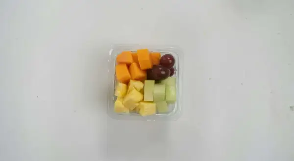 Pudełko z pokrojonymi owocami: ananas, melon, papaja i winogrona. Idealna przekąska, jeśli zastanawiasz się, czy mus owocowy można do samolotu.