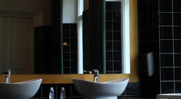 Elegante bagno nero design con due lavabi bianchi, rubinetteria cromata e specchio dorato. Pareti rivestite di piastrelle nere lucide.