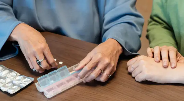 Dwie osoby sortują tabletki w pojemniku na leki. Dostępne są darmowe leki dla seniorów.