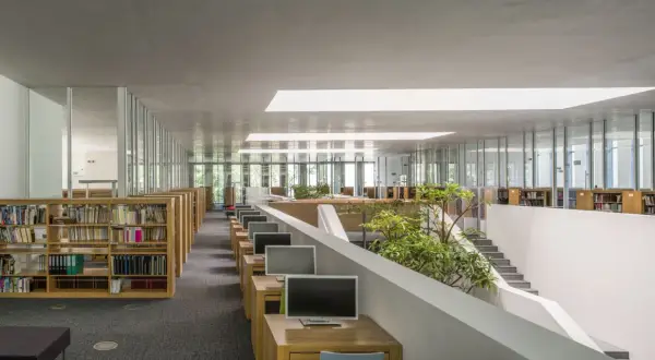 Nowoczesne wnętrze biblioteki Raczyńskich z rzędami regałów, komputerami i zielenią.