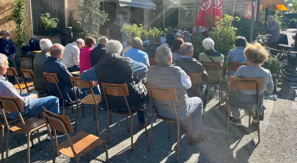 Un gruppo di persone ascolta un relatore durante un tricot cafè tutorial all'aperto.