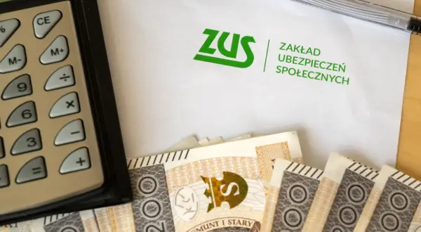 Kalkulator, banknoty i dokument ZUS. Obrazek nawiązuje do tematu zasiłku przedemerytalnego i finansów.