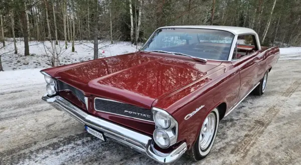 Röd Pontiac 60-tal, en klassisk bil med kromdetaljer, står parkerad i snöig skogsmiljö.