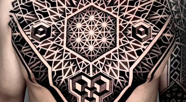 Ein komplexes Tattoo mit geometrischen Mustern bedeckt die Brust und den Arm. Es zeigt verschachtelte Hexagone, Würfel und stilisierte Dreiecke.