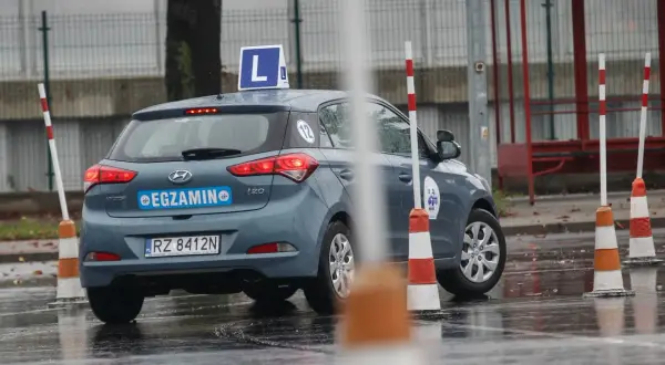 Szary Hyundai i20 z literą "L" na dachu i napisem "EGZAMIN" na klapie, gotowy do jazdy próbnej.