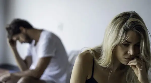 Smutna kobieta i zamyślony mężczyzna siedzą na łóżku. W ich relacji panuje napięcie, trudno im zaufać.