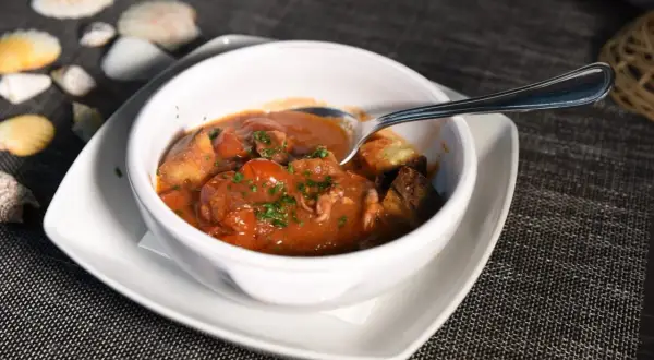 Polipetti in purgatorio, un piatto di mare con pomodorini e pane tostato, servito in una ciotola bianca su un tavolo scuro.