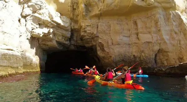 Kayakistas exploran las impresionantes cuevas de Cabo de Gata, navegando por aguas cristalinas bajo acantilados dorados.