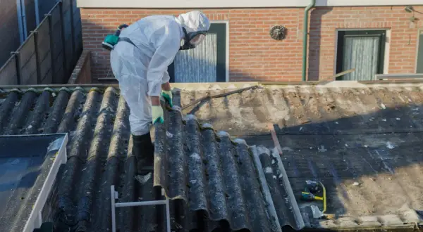 Pracownik w kombinezonie ochronnym usuwa eternit z dachu, dbając o bezpieczeństwo przy pracy z materiałem zawierającym azbest.