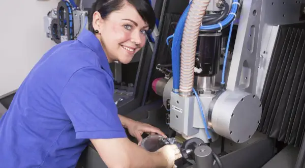 Frau mit blauen Polohemd arbeitet an einer CNC-Maschine. Sie vertieft sich in ihre Weiterbildung als Zerspanungsmechanikerin.