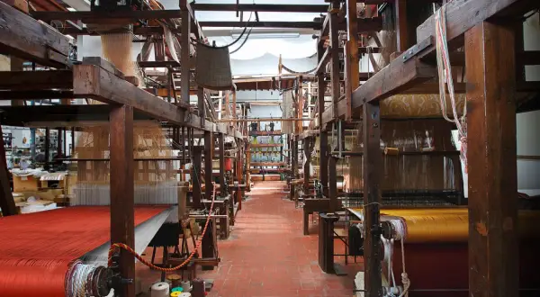 Interno di un antico setificio fiorentino con telai in legno e tessuti colorati.