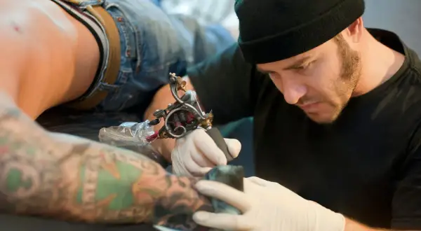 Artista de tatuajes concentrado, considerado el mejor del mundo, trabajando en un brazo con diseño detallado.
