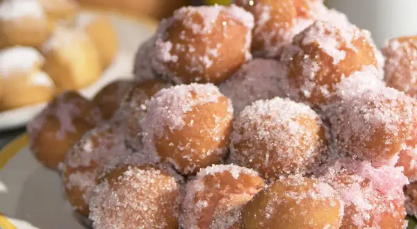 Castagnole marchigiane ricetta originale: dolcetti fritti dorati, cosparsi di zucchero semolato e un tocco di zucchero rosa.