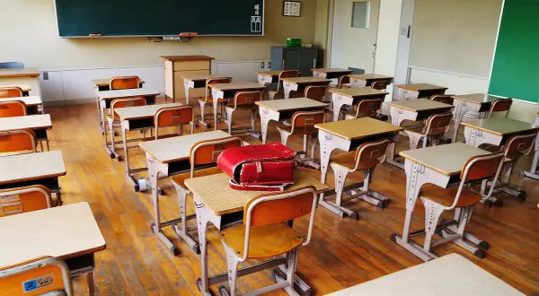 Pusta klasa z rzędami ławek i krzeseł, gotowa na lekcje w szkole dla dzieci z autyzmem. Czerwony tornister leży na jednej z ławek.