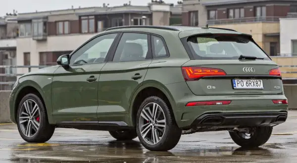 Zielony Audi Q5 Sportback na mokrym parkingu, z budynkami w tle.