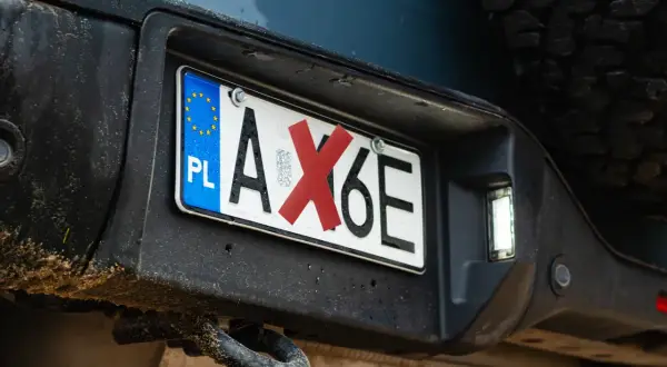 Polski numer rejestracyjny pojazdu AX6E z czerwoną naklejką na literze X.