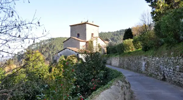 Strada panoramica verso Sant'Andrea di Compito, con un antico borgo in pietra e vegetazione rigogliosa.