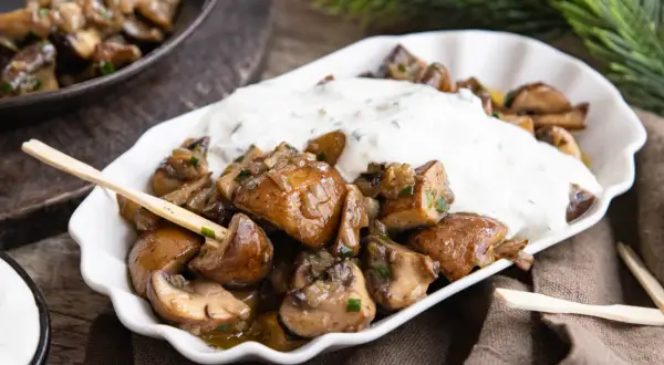 Gebratene Champignons mit Kräuterquark, wie vom Weihnachtsmarkt, auf einem weißen Teller mit Holzspießen.