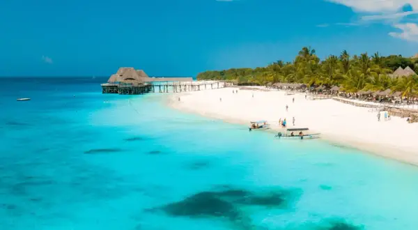 Rajskie zanzibar wakacje: biała plaża, palmy, turkusowa woda i drewniany pomost z domkami na wodzie. Idealne miejsce na relaks.