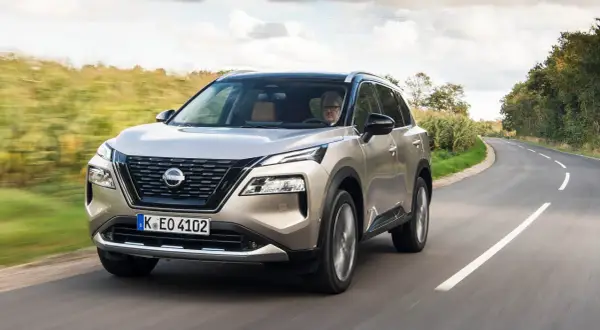 En man kör en beige Nissan X-Trail på en kurvig landsväg. Inga problem syns med bilen.