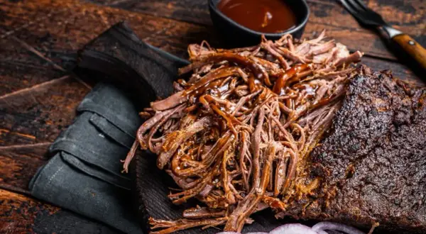 Soczysta, wolno pieczona szarpana wołowina z sosem BBQ, podana na desce z cebulą. Idealna na grilla.