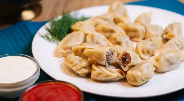 Pyszne pierogi z gęsiną, podane z ziołowym dipem i sosem pomidorowym, ozdobione gałązką koperku.