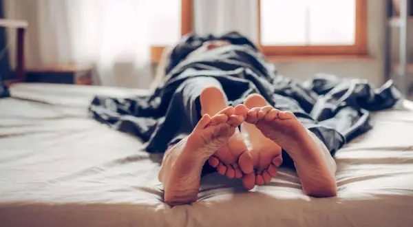 Zwei Füße berühren sich unter einer Decke. Ein Paar, das sich an die Regel "kein Sex vor der Ehe" hält, genießt die Nähe.