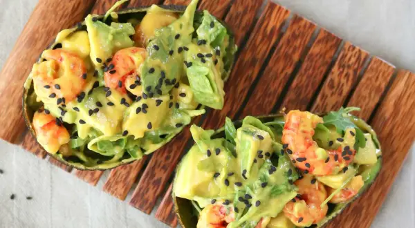 Deliciosa ensalada de langostinos y aguacate, servida en mitades de aguacate y espolvoreada con semillas de sésamo negro.