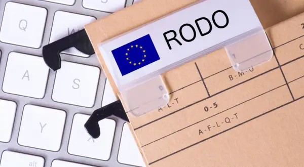 Dokumentacja RODO na teczce z etykietą "RODO" i flagą UE, leżąca na klawiaturze. To rejestr czynności przetwarzania.