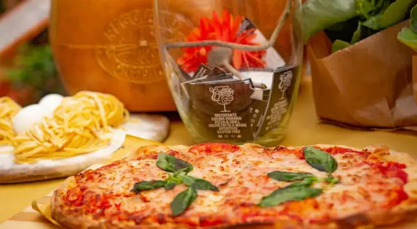 Pyszne rodzaje pizzy, makaron i ser parmezan. W tle szklany wazon z dekoracjami i kwiaty.