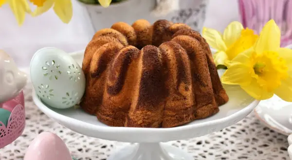 Wilgotna babka wielkanocna dwukolorowa, ozdobiona wielkanocnymi pisankami i żółtymi żonkilami, zapowiada wiosenne święta.