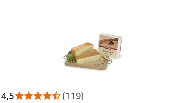 Due fette di formaggio tipo taleggio su tagliere di legno con uva e confezione.