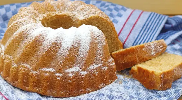 Puszysta babka z owocami, oprószona cukrem pudrem, czeka na spróbowanie. Obok leżą dwa kawałki ciasta.