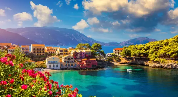 Piękna kefalonia pogoda czerwiec: kolorowe domki nad turkusową zatoką, góry w tle, kwitnące kwiaty na pierwszym planie.