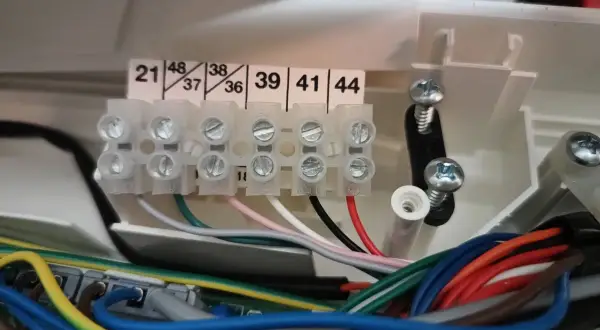 Zaciski elektryczne z numerowanymi wejściami i wiązką kolorowych przewodów.