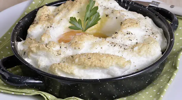 Delicioso huevo al horno, con clara montada y yema cremosa, adornado con perejil y pimienta.