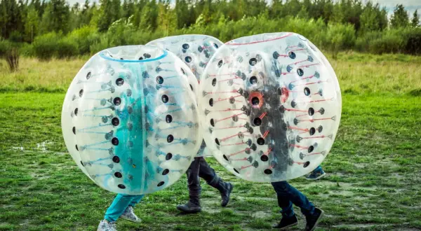 Tre personer i genomskinliga bubblor, redo för bumperball hyra. En rolig utomhusaktivitet med mycket skratt.