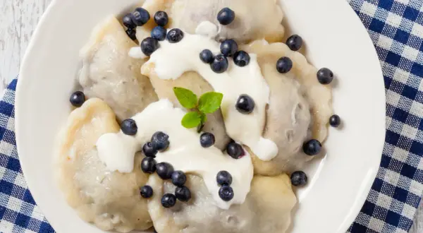 Pyszne pierogi z jagodami, polane śmietaną i posypane świeżymi owocami. Idealne na letni deser.