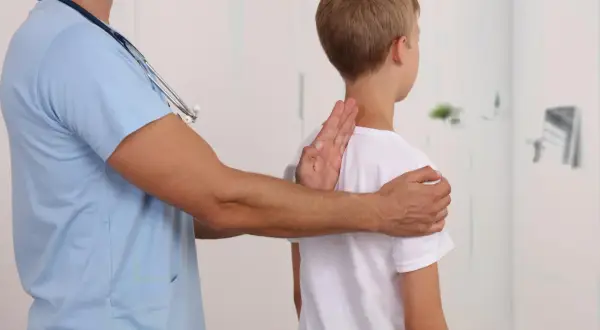 Lekarz bada chłopca, sprawdzając jego postawę. Może to być część diagnostyki zespołu Marfana, gdzie obserwuje się różne objawy.