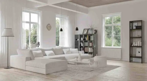 Soggiorno luminoso con divano bianco, libreria e finestre ampie. Un esempio di come dipingere una stanza per farla sembrare più grande, usando colori chiari e arredi minimalisti.