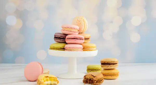 Bunte Macarons, frisch gebacken, stapeln sich auf einem weißen Tortenständer. Einige sind angeknabbert und zeigen ihre cremige Füllung.