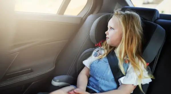 Ein blondes Mädchen sitzt im Kindersitz und schaut aus dem Fenster. Die Frage "wie lange Kindersitz" beschäftigt viele Eltern.