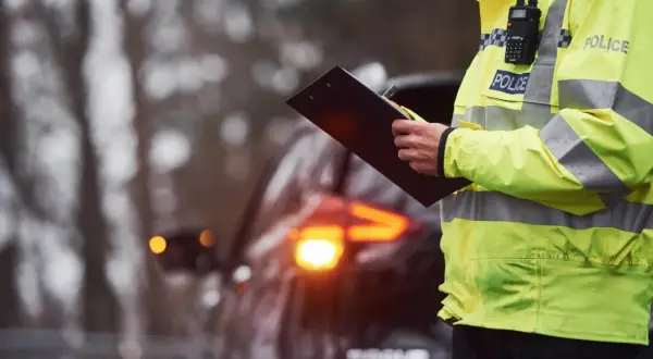 Policjant w kamizelce odblaskowej z napisem "POLICE" spisuje mandaty na Słowacji. W tle widać samochód z włączonymi światłami awaryjnymi.