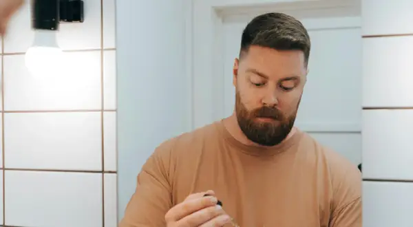 Visage homme 50 ans, barbe rousse, tenant un compte-gouttes.