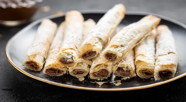 Rotolini croccanti di pasta fillo ripieni di cioccolato, spolverati di zucchero a velo.