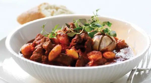 En skål med mustig chili con carne, garnerad med färska örter och en hel vitlöksklyfta. En bit bröd syns i bakgrunden.