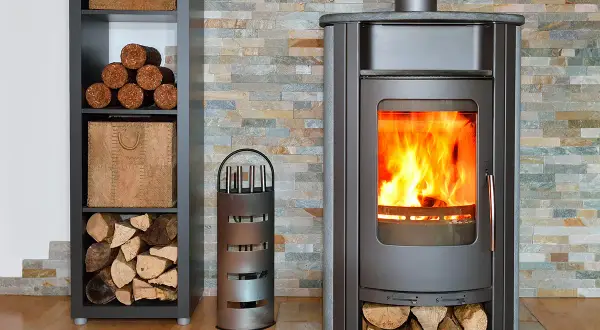 Un poêle à bois crépitant, avec du bois rangé à côté. Un accessoire pour le feu est présent.