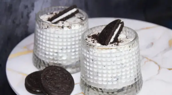 Dwa deserki z kremem i pokruszonymi oreo ciastkami, ozdobione połówkami ciastek.