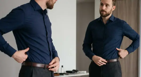 Mann steckt sein blaues Hemd richtig in die Hose, um einen gepflegten Look zu erzielen.