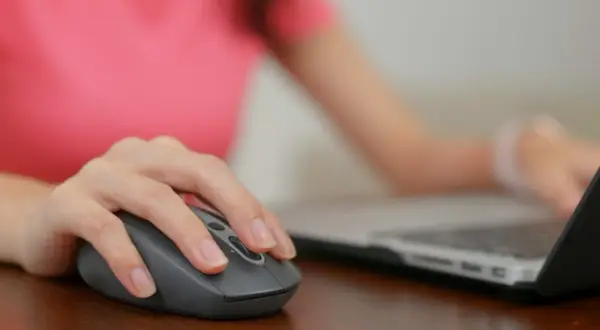 Dłoń na myszce, która jest podłączona do laptopa. Wiesz już, gdzie podłączyć myszkę do komputera.